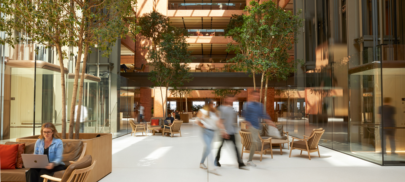 La planta baja del atrio de Battersea, bañada por la luz del sol y con diferentes personas de Apple reunidas, caminando y charlando en diferentes espacios.