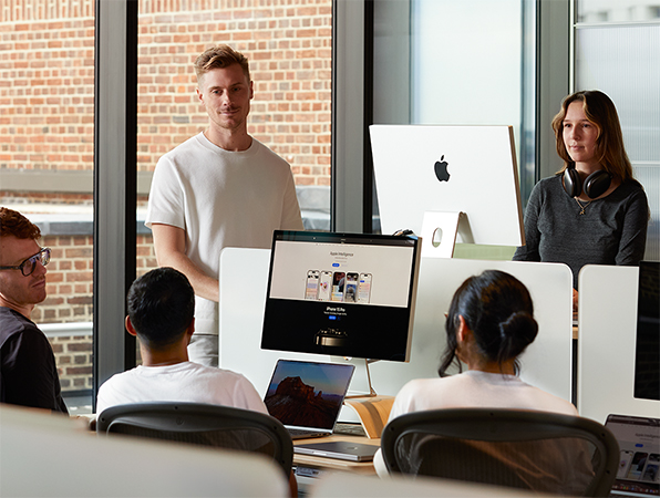 Cinco empleados de Apple charlando alrededor de sus ordenadores.