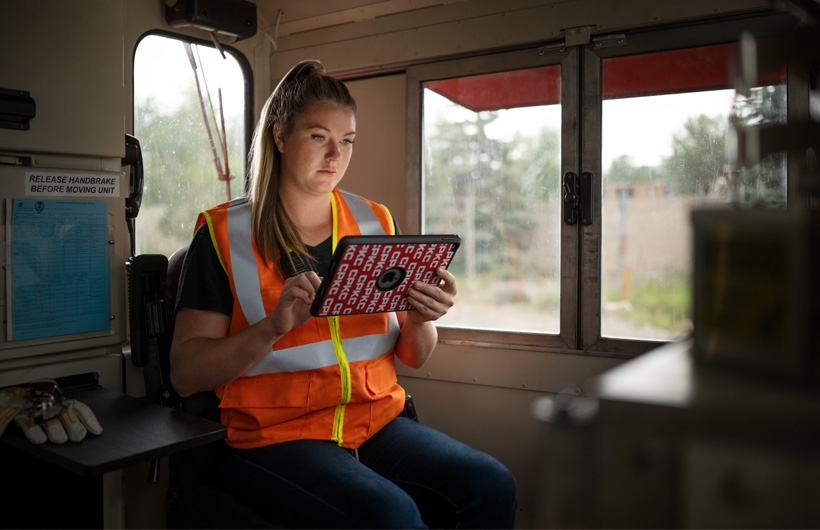 En järnvägsarbetare sitter i en stillastående tågvagn och läser information på en iPad