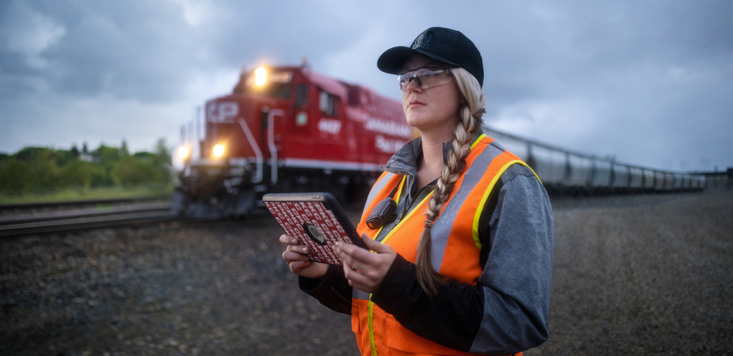Trabalhadora ferroviária segura um iPad e verifica os carris enquanto passa um comboio